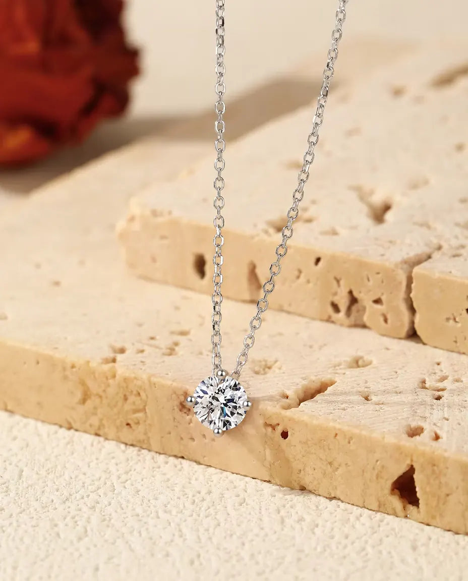 1 ct Moissanite Solitaire Necklace in 925 Sterling Silver - pendant hanging over the edge of a travertine slab
