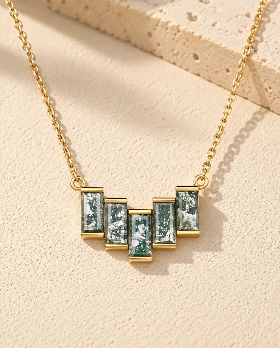 Moss Agate Baguette Necklace in 10K Gold Plated 925 Sterling Silver - lying on a cream textured surface beside a travertine block
