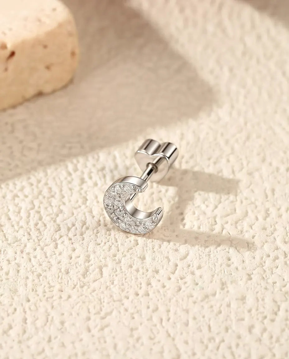 Pavé Moissanite Crescent Stud Earrings in 925 Sterling Silver - lying on its side on a cream textured surface, heart-shaped back on the post