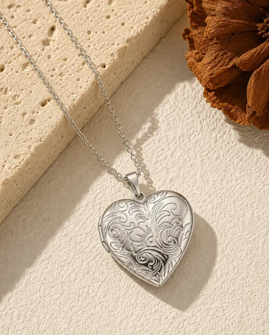 Personalised silver heart photo locket necklace with engraved floral front in warm flat-lay scene