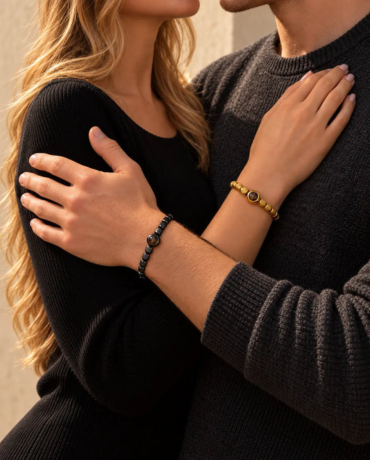 Couple in an embrace, she wears the gold tone projection bead bracelet and he wears the black one