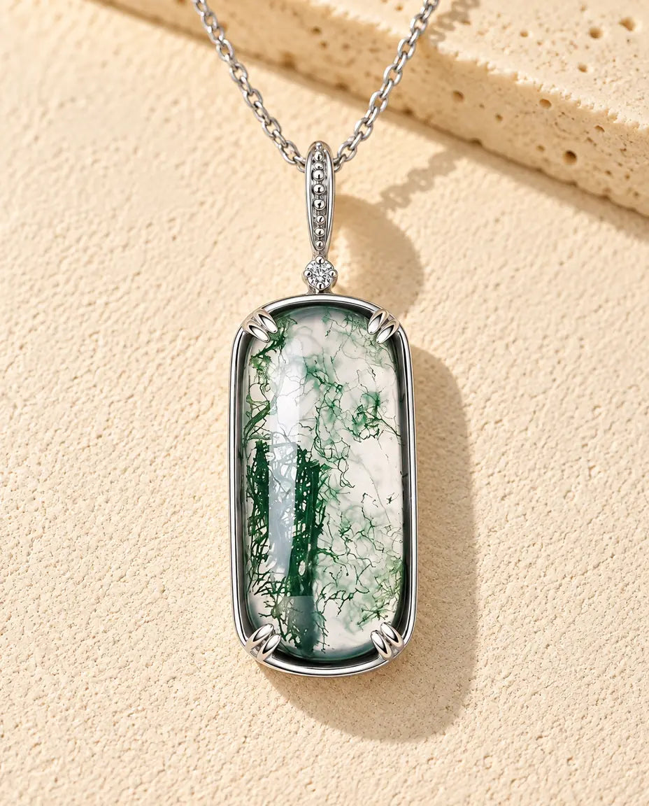 Rectangle Moss Agate Pendant Necklace in 925 Sterling Silver - lying on a cream textured surface beside a travertine block