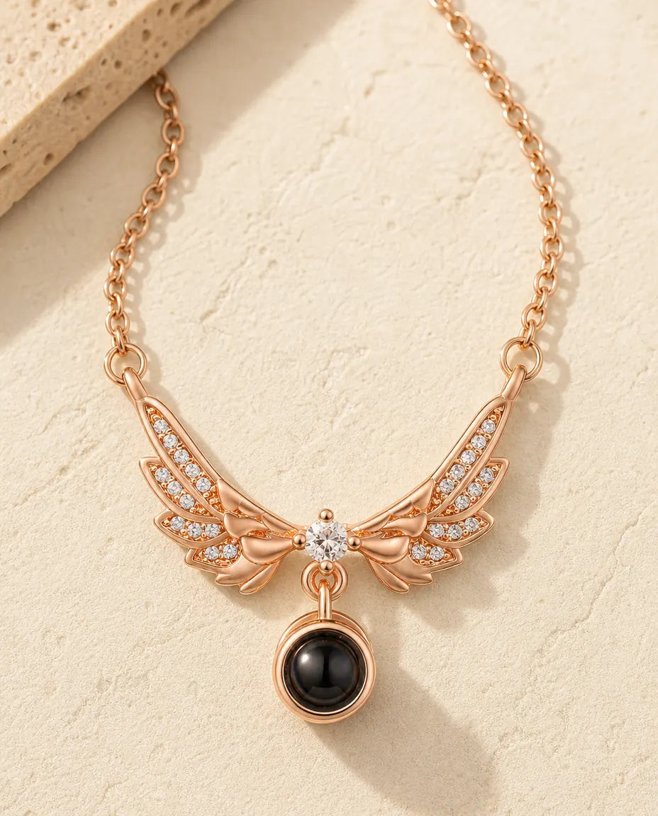 Rose gold angel wing photo projection necklace on a warm cream stone surface