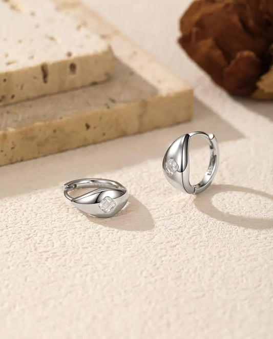 Asscher Cut Moissanite Huggie Hoop Earrings in 925 Sterling Silver - pair on a cream textured surface, one lying flat and one standing