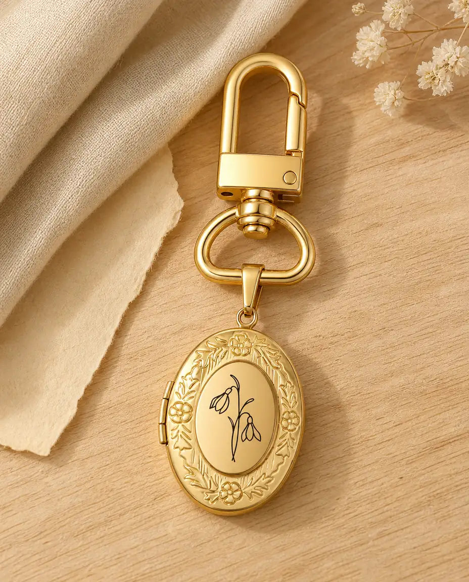 Gold birth flower photo locket keyring engraved with a snowdrop on a wood table