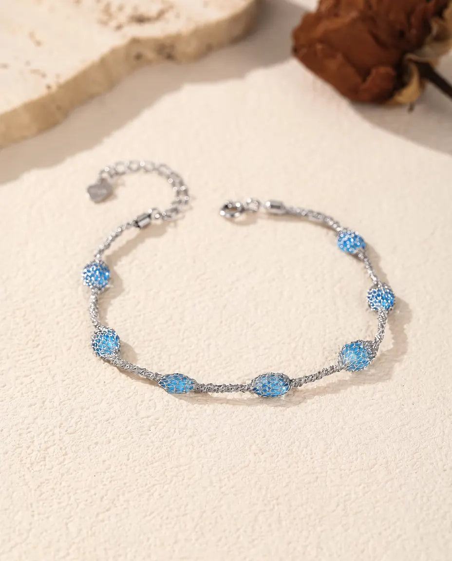 Caged Zircon Bracelet in 925 Sterling Silver - blue zircon version laid flat on a cream surface