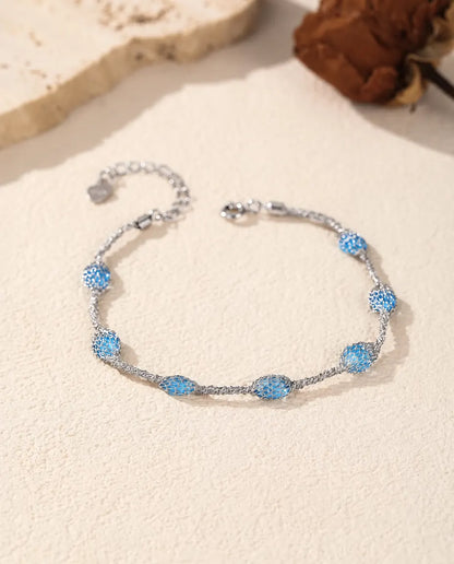 Caged Zircon Bracelet in 925 Sterling Silver - blue zircon version laid flat on a cream surface