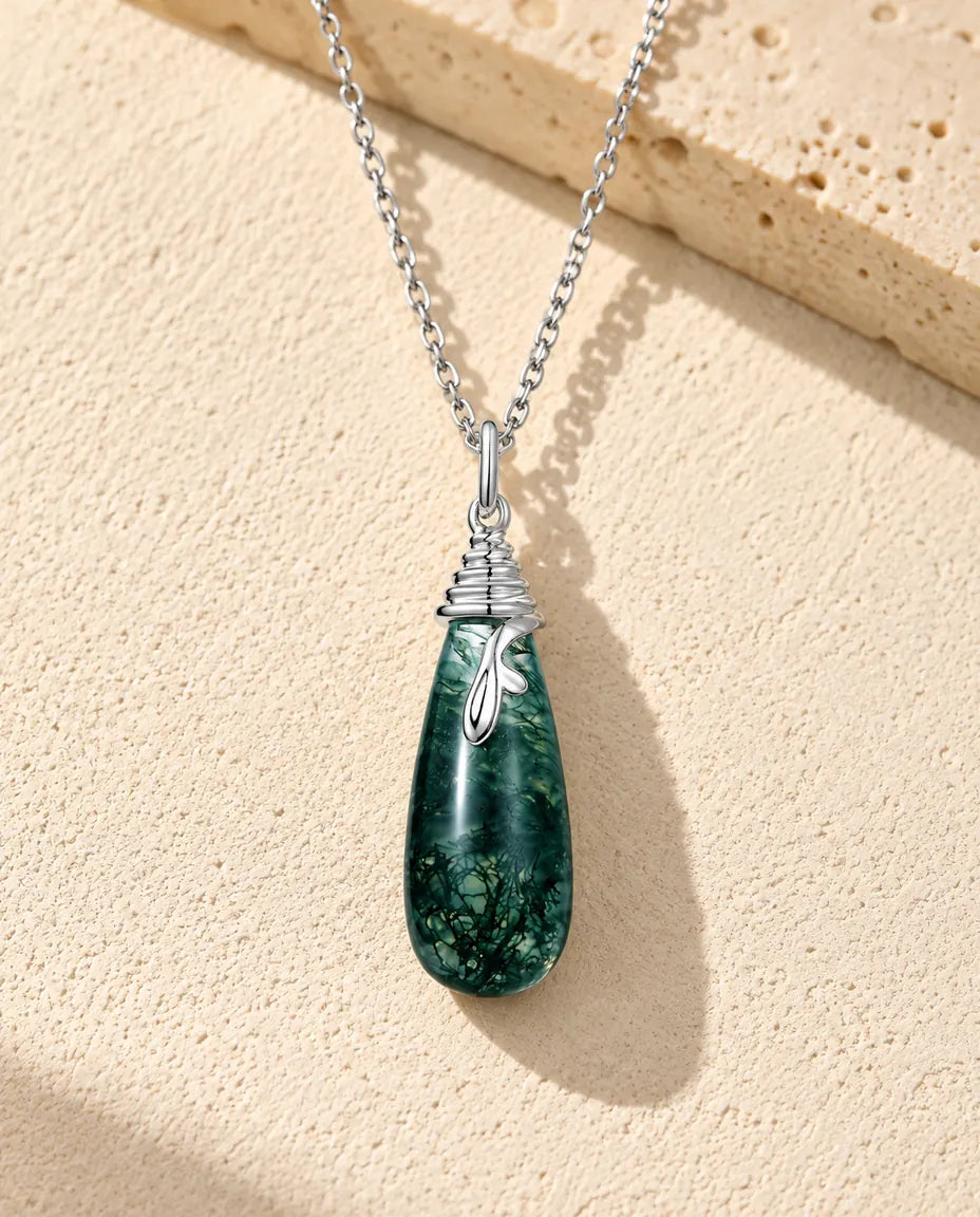 Moss Agate Teardrop Necklace in 925 Sterling Silver - lying on a cream textured surface beside a travertine block
