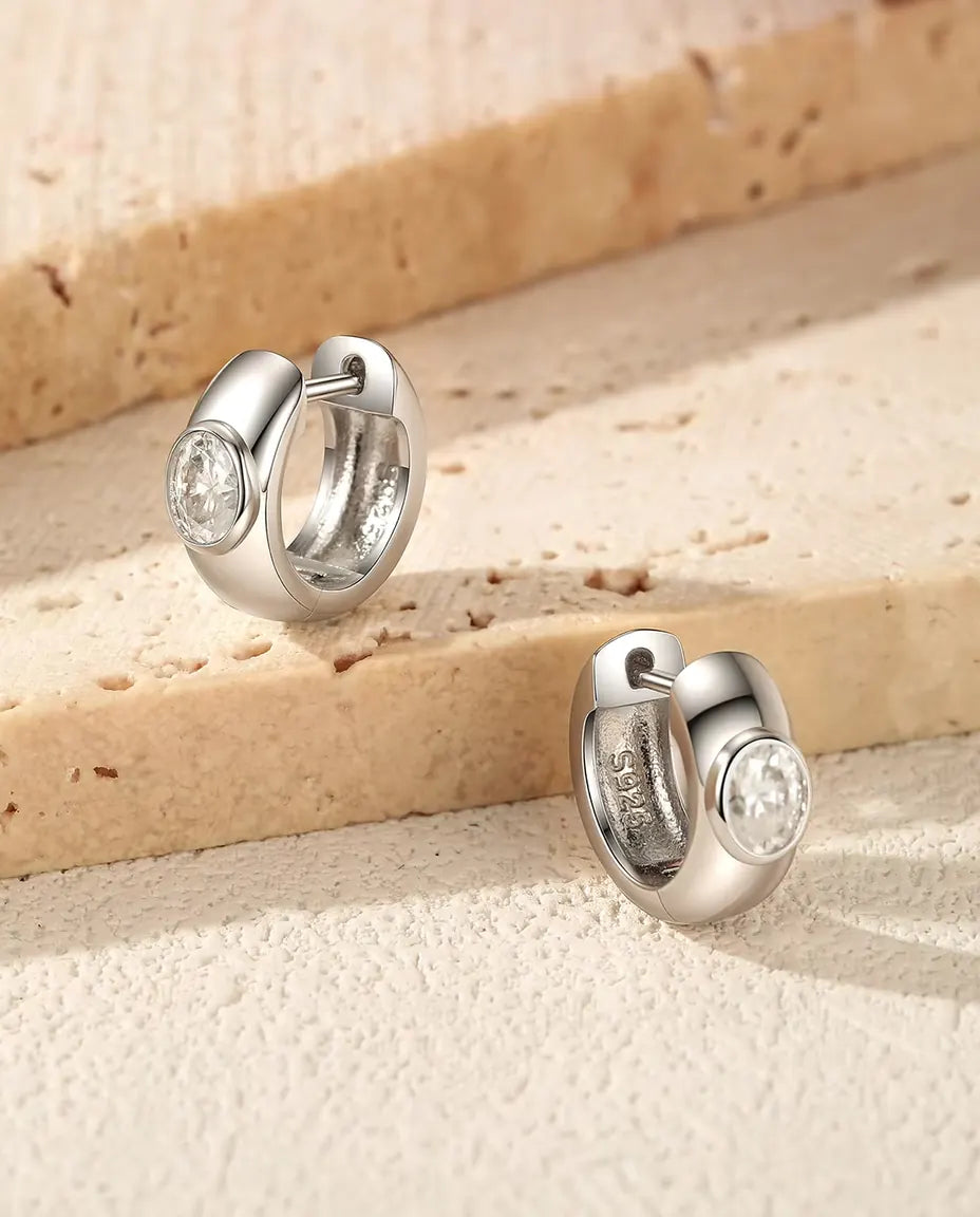 Oval Moissanite Huggie Hoop Earrings in 925 Sterling Silver - the pair resting on travertine steps