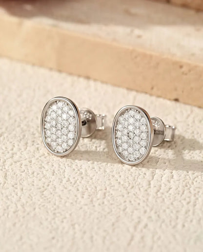 Oval Pave Moissanite Stud Earrings in 925 Sterling Silver - the pair lying on a cream textured surface