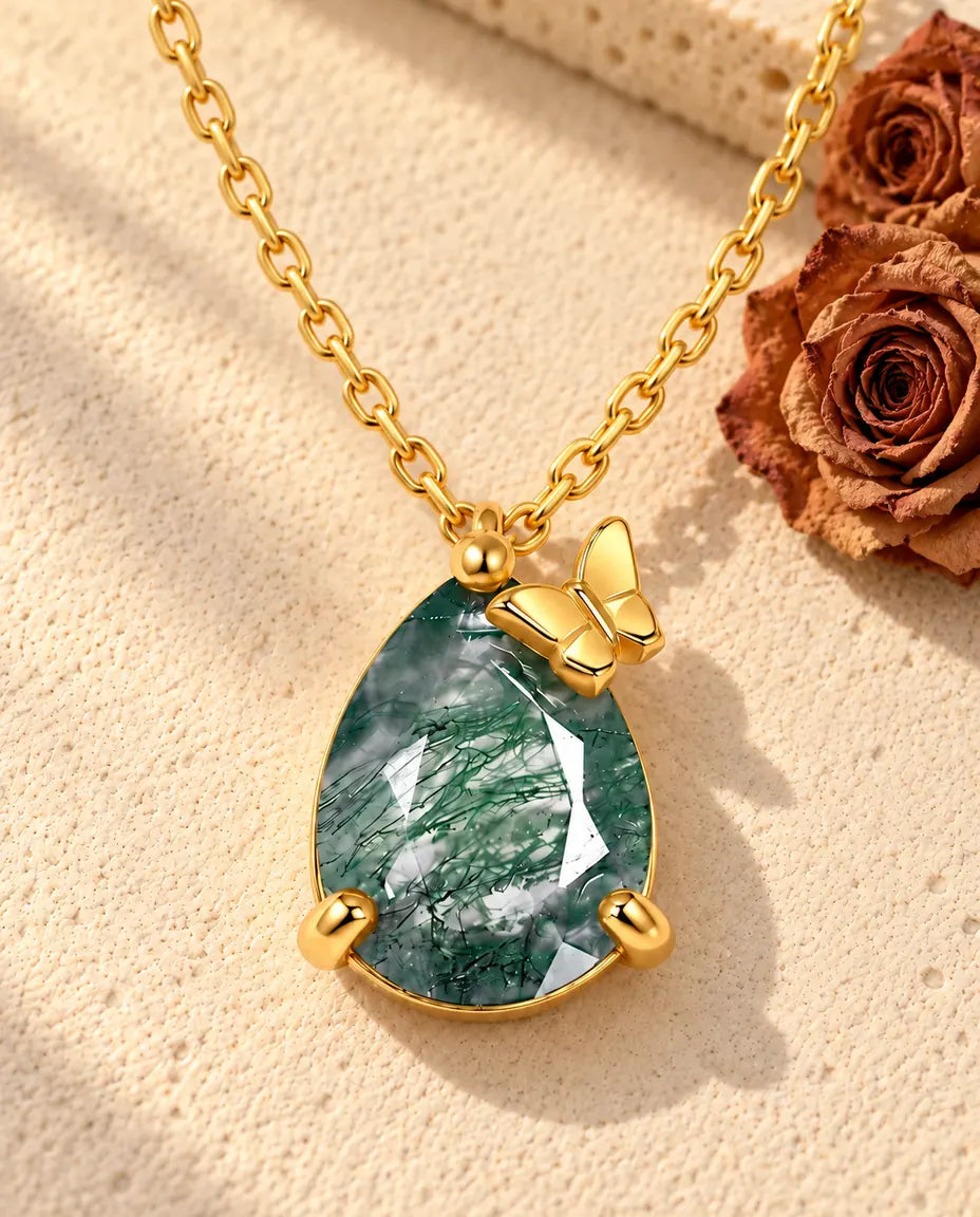 Pear Moss Agate Butterfly Necklace in 10K Gold Plated 925 Sterling Silver - lying on a cream textured surface beside a travertine block