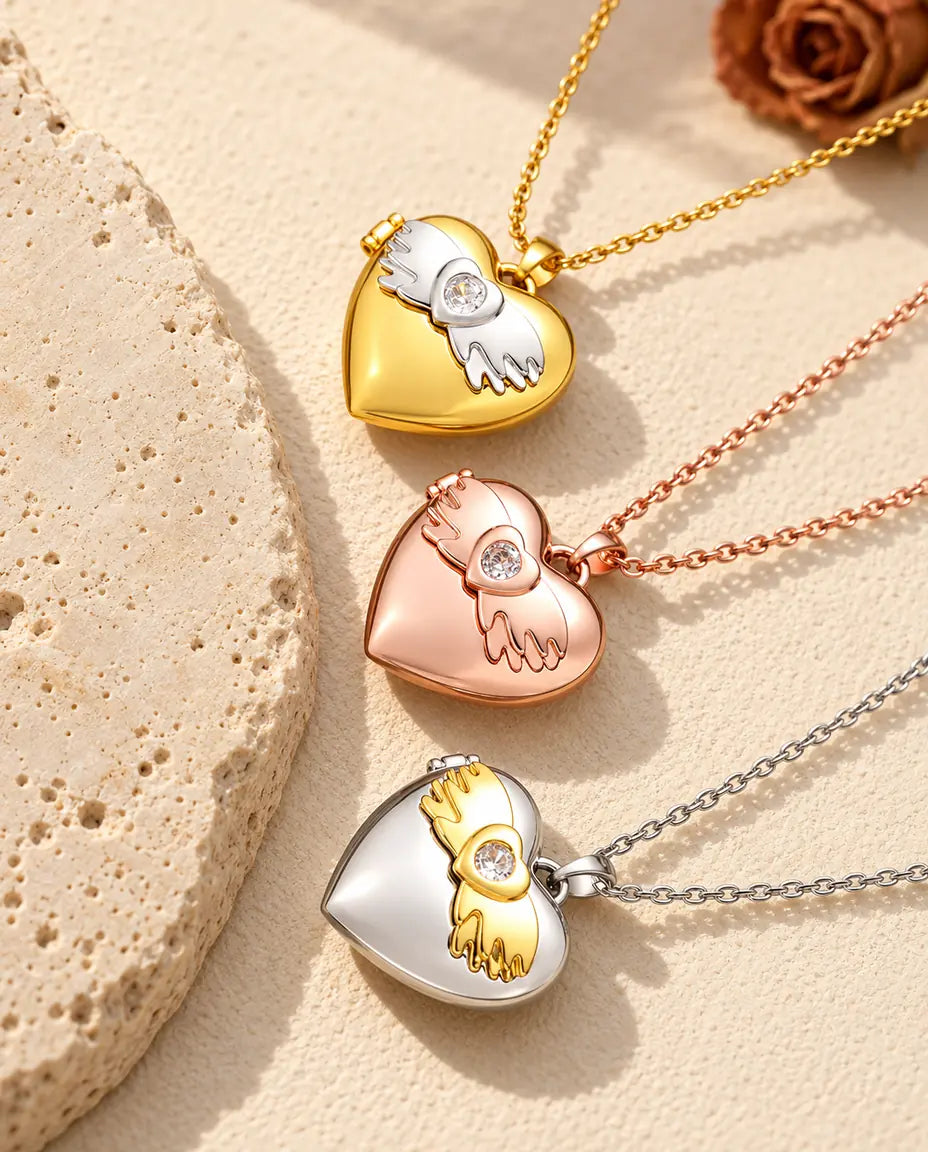 Gold tone, rose gold tone and silver tone angel wings heart photo lockets stacked beside a travertine slab