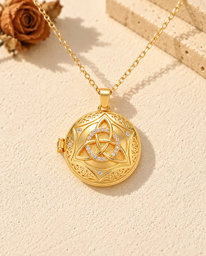 Front view of the gold tone round locket showing the trinity knot, four-pointed star and side hinge