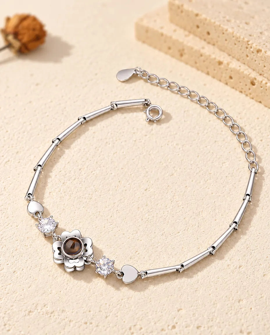 Personalised clover flower photo projection bracelet in silver tone on a slim bar chain, lying on cream plaster