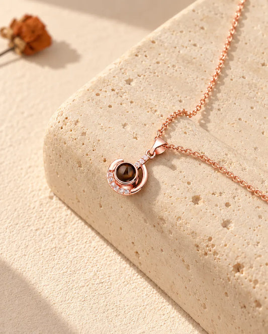 Personalised rose gold tone crescent moon photo projection necklace on a travertine block