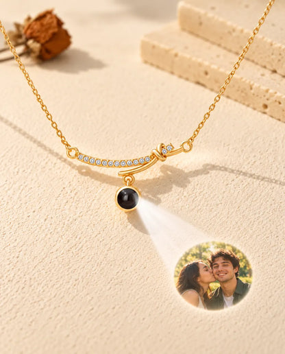 Gold tone curved bar necklace projecting a couple photo onto cream plaster