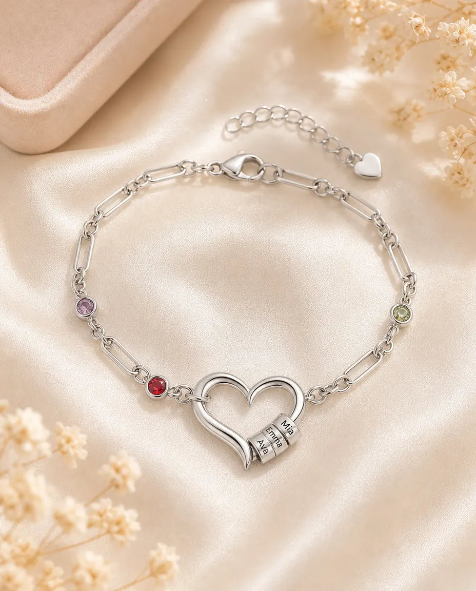 Personalised silver name bracelet with an open heart and birthstones, flat lay on cream silk