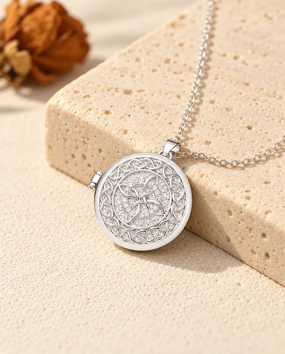 Personalised four-loop Celtic knot photo locket necklace in silver tone with a ring of cubic zirconia, resting on a travertine block