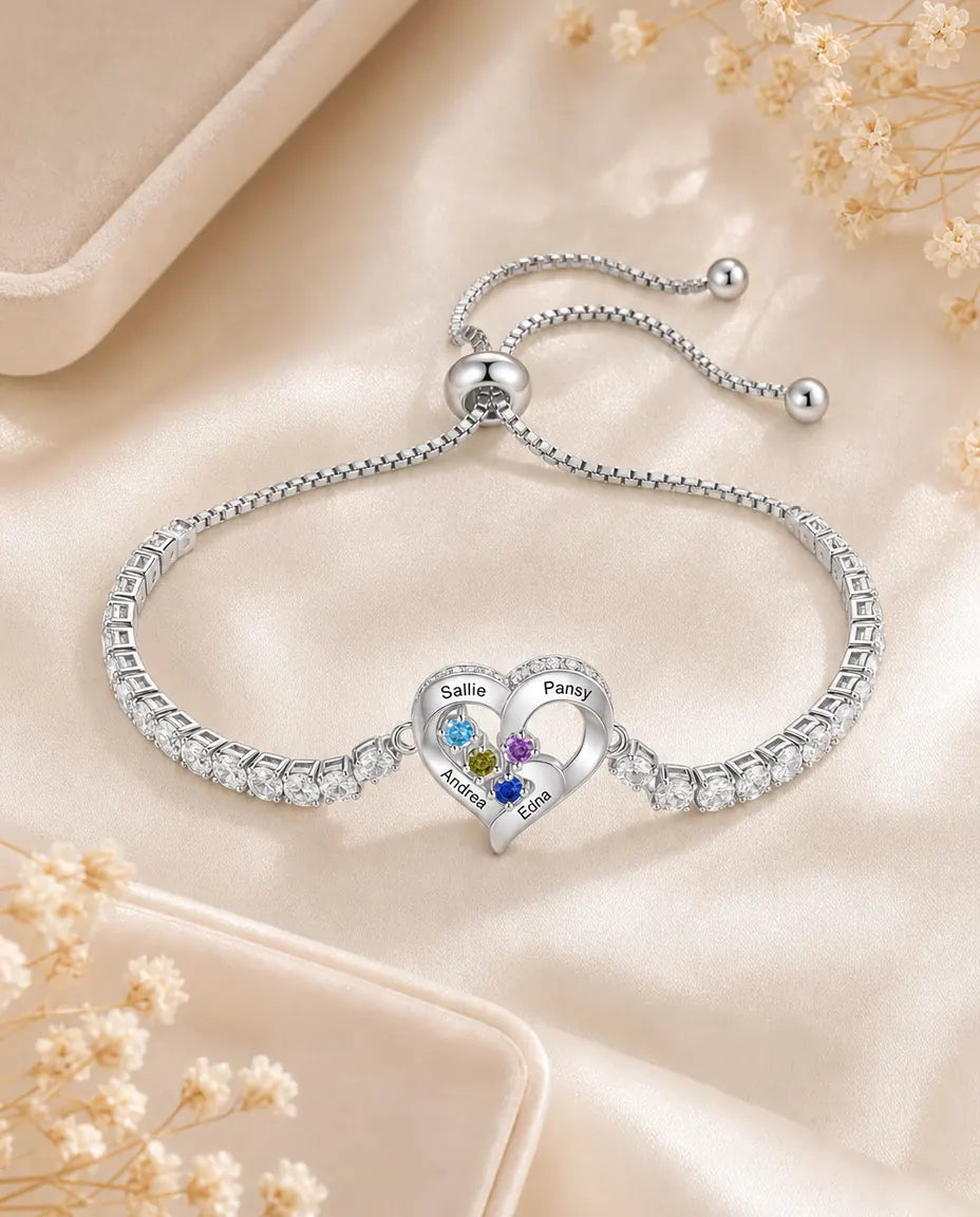 Personalised heart tennis bracelet with engraved names and birthstones, flat lay on cream silk