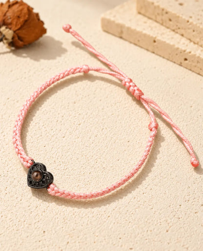 Pink thin braided cord bracelet with a black heart charm holding a brown projection stone
