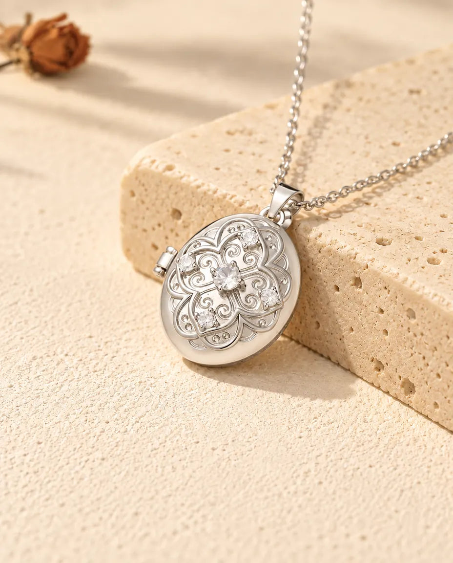 Personalised oval photo locket necklace in silver with a filigree flower lid and cubic zirconia, resting on a travertine block