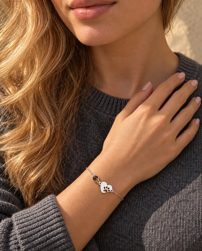 Woman with her fingertips at her collarbone wearing the silver tone paw print heart projection bracelet