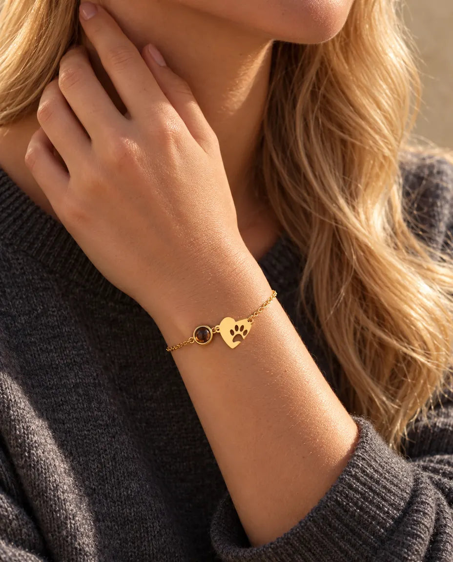 Close-up of the gold tone paw print heart bracelet on a wrist, fingertips at the side of the neck