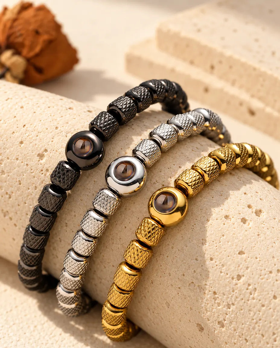 Three bead bracelets in black, silver tone and gold tone draped over a travertine block