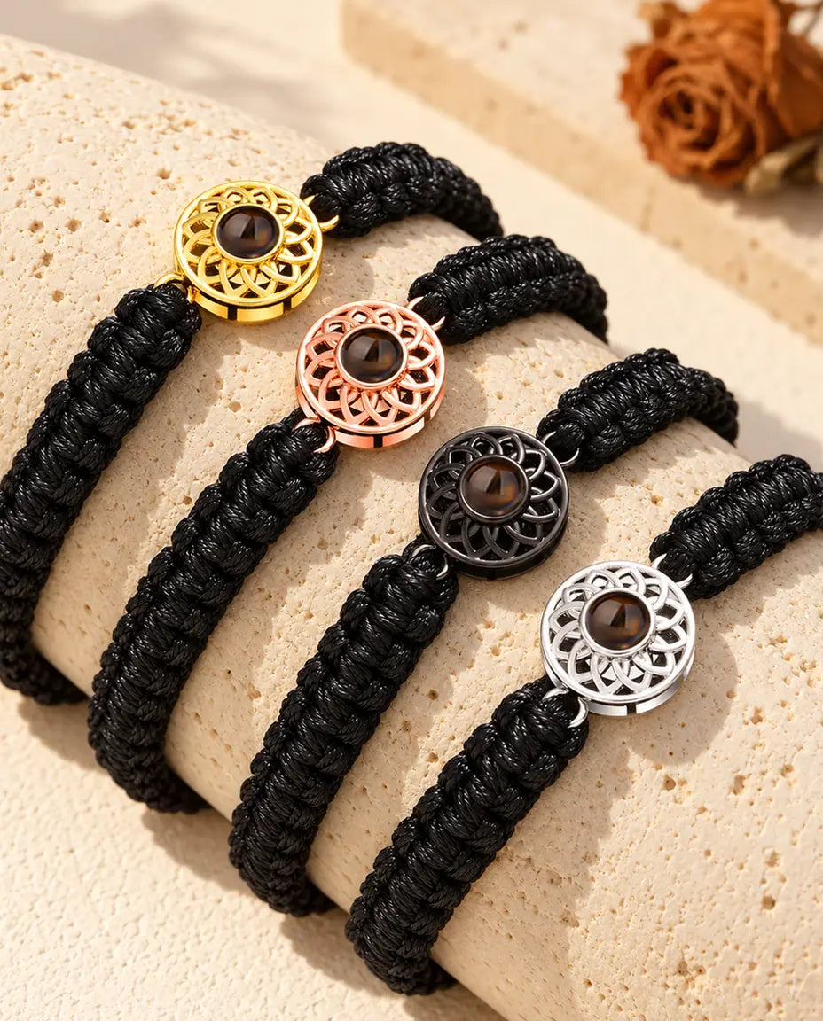 Four black braided cord bracelets showing every charm colour draped over travertine