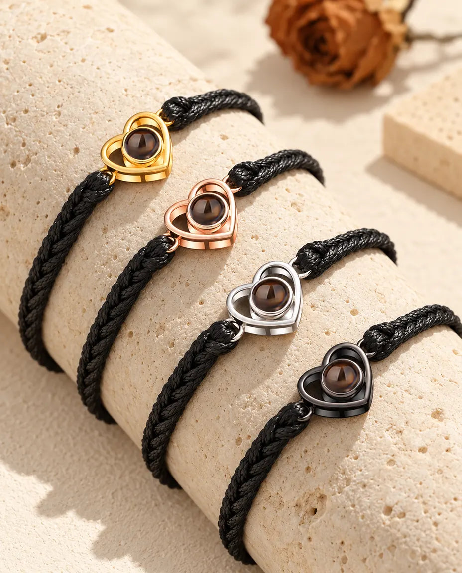 Four black braided cord bracelets with open heart charms in each colour on a travertine block