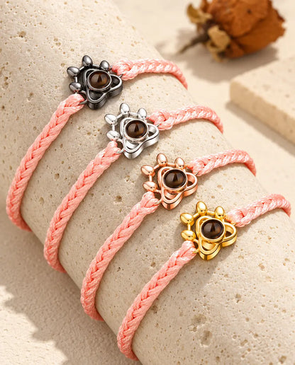 Pink braided cord paw charm bracelets showing every charm colour draped over travertine