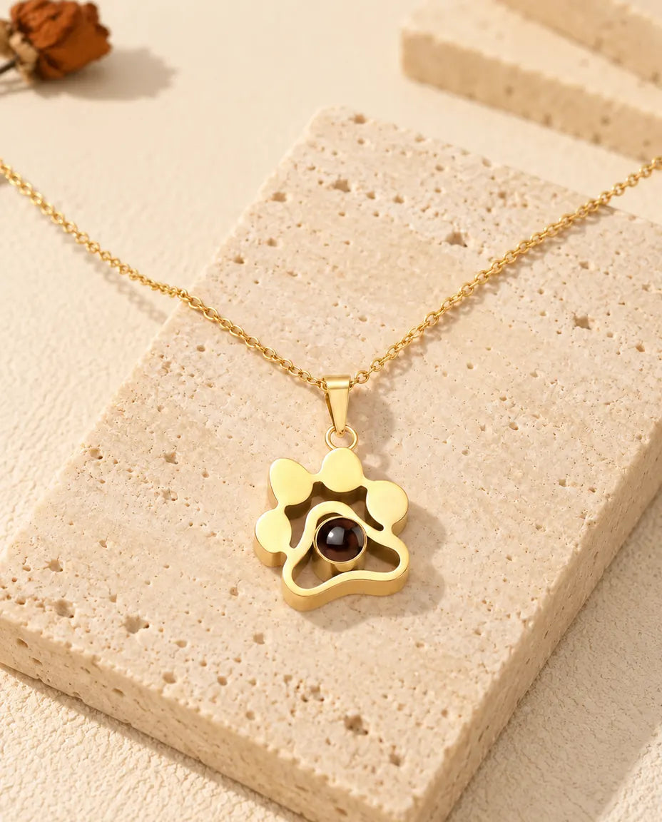 Gold tone paw print projection necklace draped over a travertine block