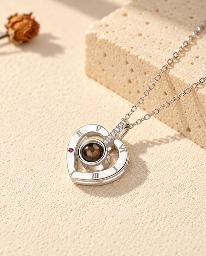 Personalised 925 sterling silver Roman numeral heart photo projection necklace on cream plaster beside travertine