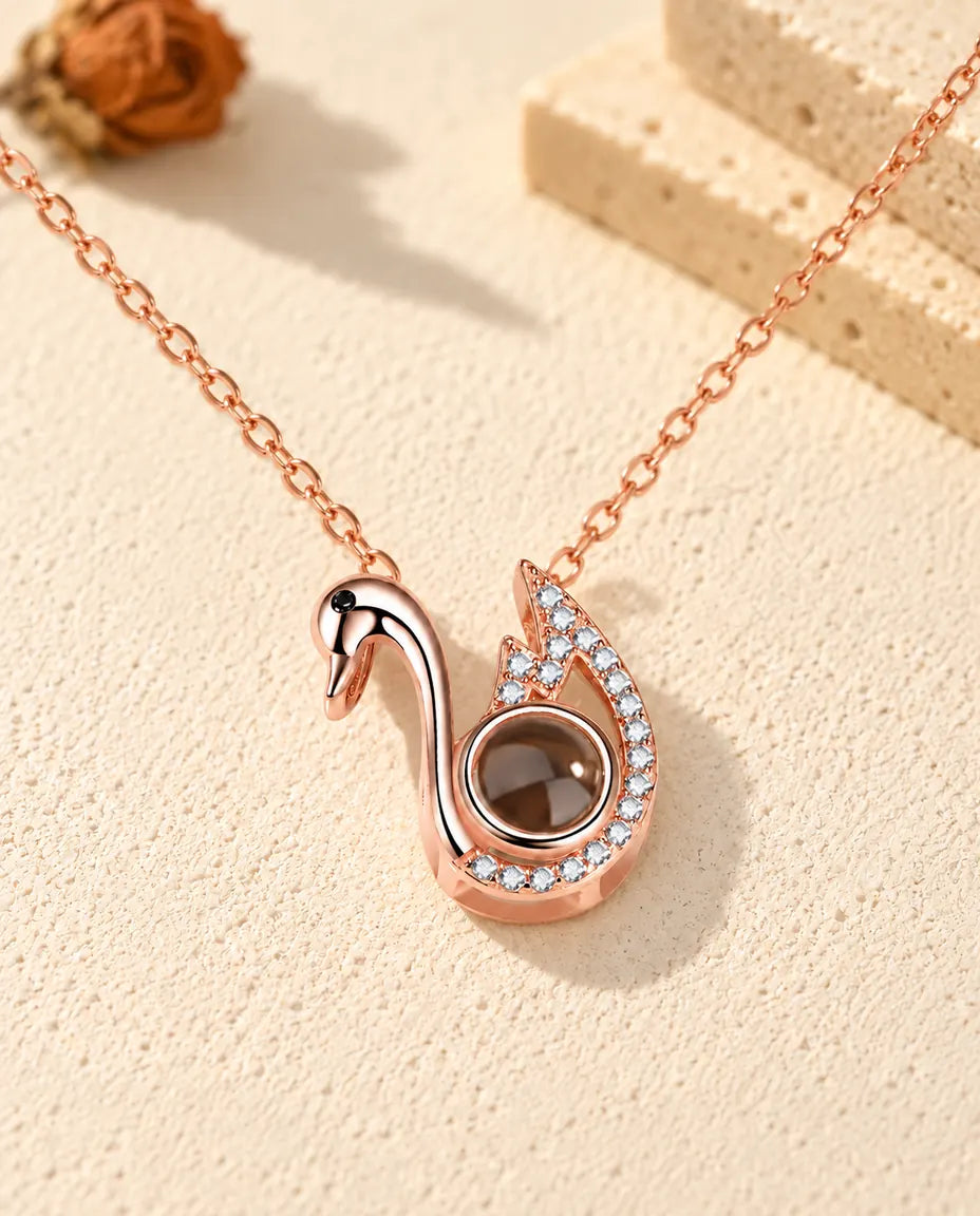 Personalised rose gold tone swan photo projection necklace on cream plaster beside travertine