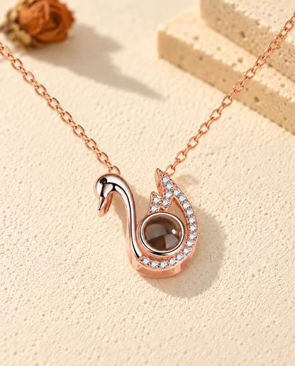 Personalised rose gold tone swan photo projection necklace on cream plaster beside travertine