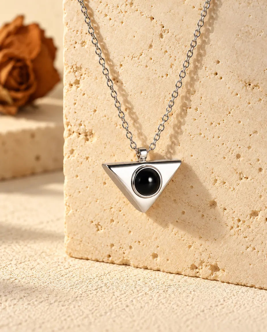 Personalised silver tone triangle photo projection necklace hanging on a travertine block