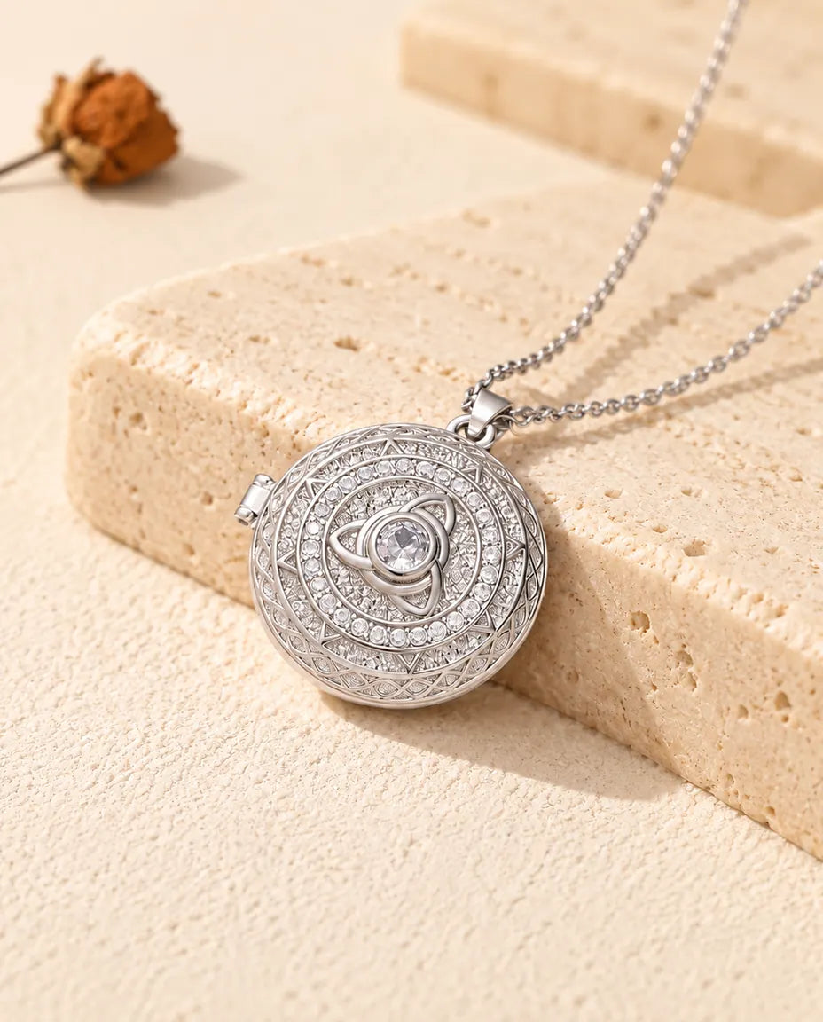 Personalised round trinity knot photo locket necklace in silver tone with cubic zirconia, resting on a travertine block