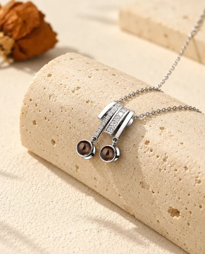 Personalised two photo projection necklace in silver tone with a pave slide and two brown projection stones on a travertine block