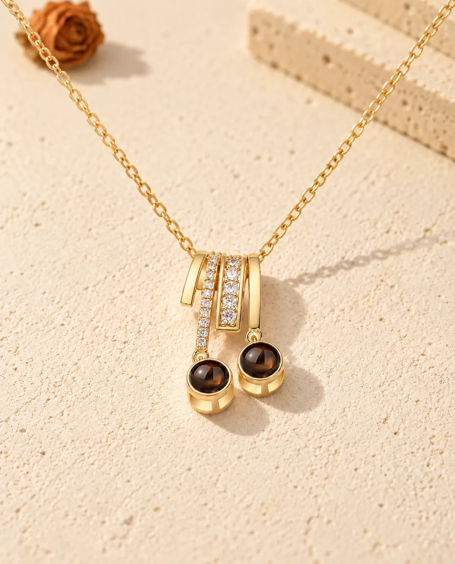 Front view of the gold tone two stone photo projection necklace on cream plaster