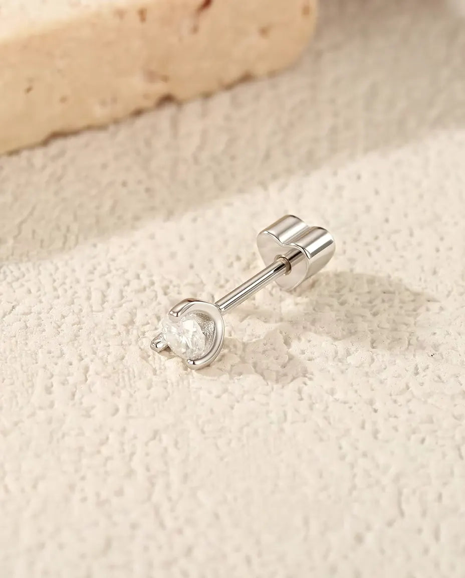 Round Moissanite Stud Earrings in 925 Sterling Silver - lying on its side on a cream textured surface, heart-shaped back on the post