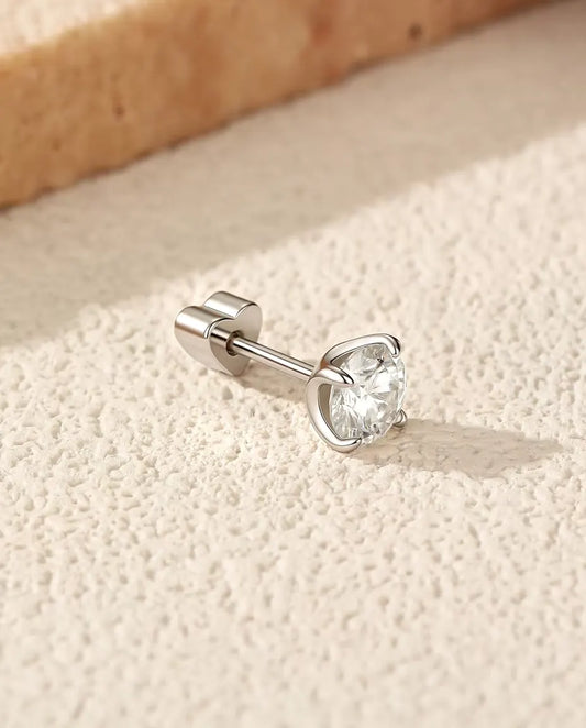 Round Moissanite Four-Prong Stud Earrings in 925 Sterling Silver - lying on its side on a cream textured surface, heart-shaped back on the post