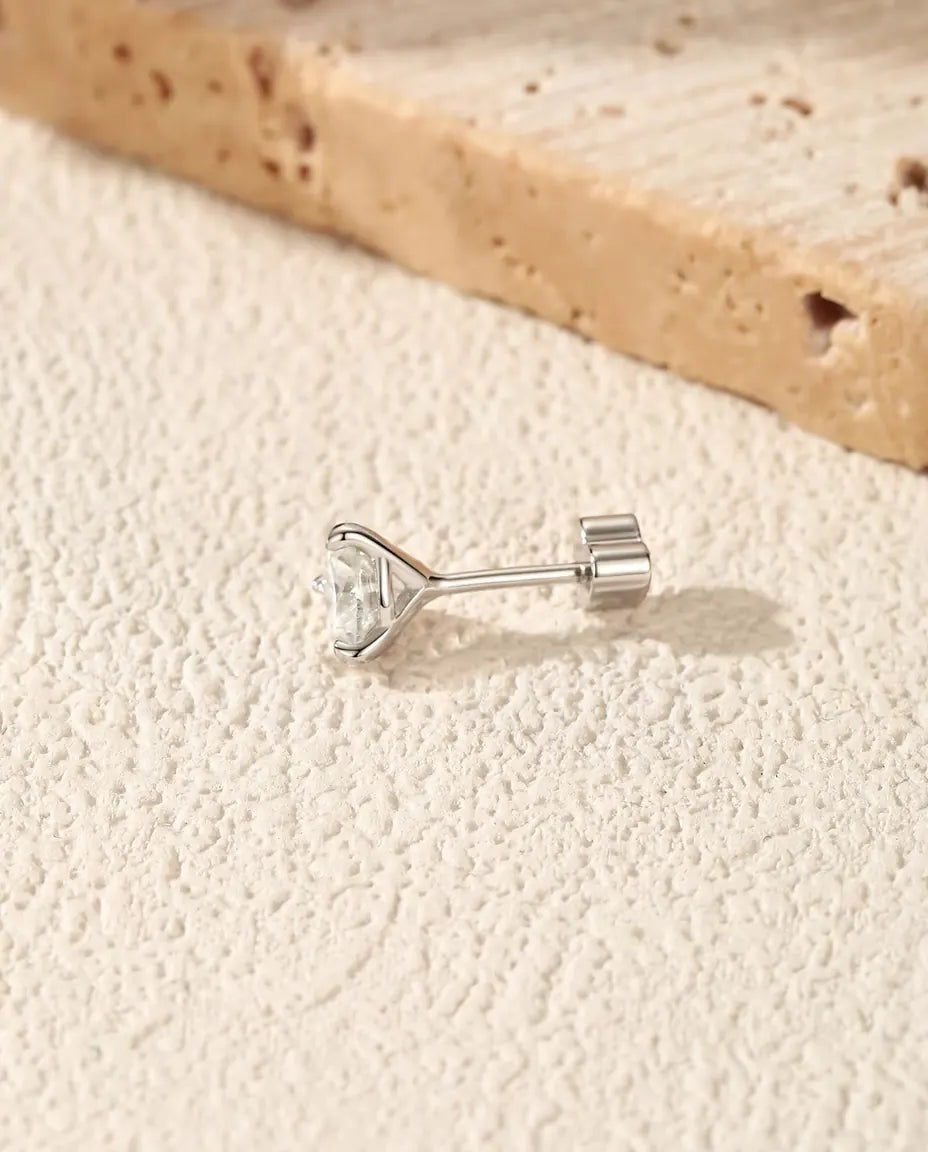 Round Moissanite Three-Prong Stud Earrings in 925 Sterling Silver - lying on its side on a cream textured surface, heart-shaped back on the post