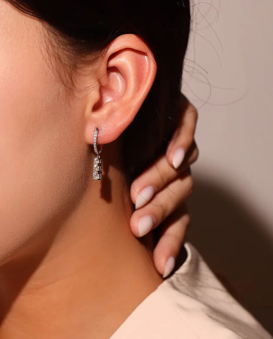 Three Stone Moissanite Drop Hoop Earrings in 925 Sterling Silver - worn on a model’s ear, fingers at her neck